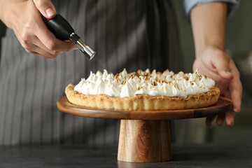 Woman toasting meringue on lemon pie with kitchen torch at table, closeup