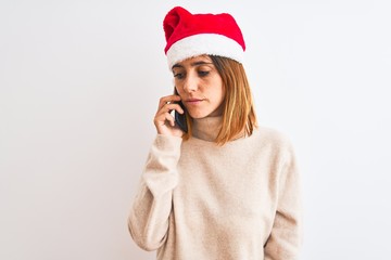 Beautiful redhead woman wearing christmas hat talking on smartphone with a confident expression on smart face thinking serious
