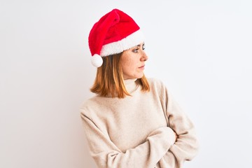 Beautiful redhead woman wearing christmas hat over isolated background looking to the side with arms crossed convinced and confident