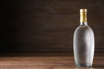 Bottle of vodka on table against wooden background. Space for text