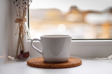 white mug of tea on the stand in front of a window on a light background