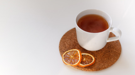 autumn juicy background. on a light white background on a wooden stand is a white mug of tea, with dried oranges and red flowers.