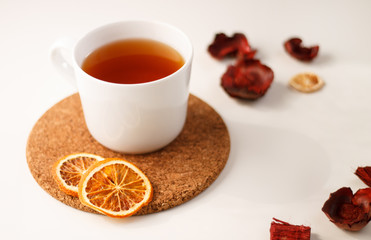 autumn juicy background. on a light white background on a wooden stand is a white mug of tea, with dried oranges and red flowers.