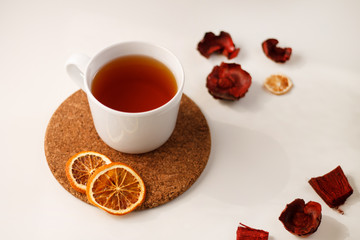 autumn juicy background. on a light white background on a wooden stand is a white mug of tea, with dried oranges and red flowers.