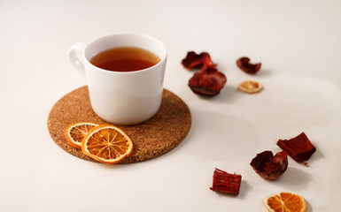 autumn juicy background. on a light white background on a wooden stand is a white mug of tea, with dried oranges and red flowers.