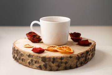 autumn juicy background. on a light white background on a wooden stand is a white mug of tea, with dried oranges and red flowers.
