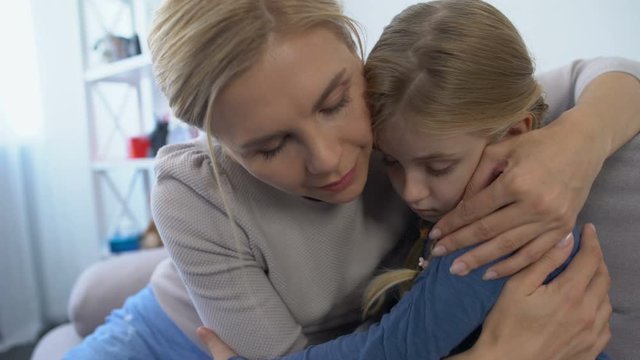 Caring mother comforting and hugging little sad daughter school bullying problem