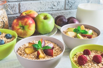 Sweet delicious healthy breakfast. Porridge with apples, plums, raspberries and blueberries on the kitchen table.