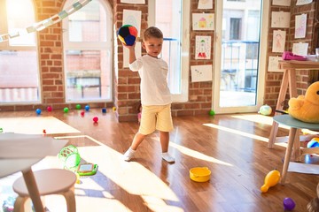 Beautiful blonde toddler standing throwing ball around lots of toys at kindergarten