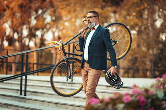 A handsome casual middle-aged businessman is going to the office by bicycle. He is carrying a bicycle on his shoulder over the stairs.