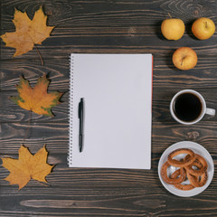 notebook with pen, autumn leaves and coffee on wooden background