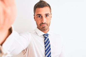 Young handsome business man taking selfie using smartphone over isolated background with a confident expression on smart face thinking serious