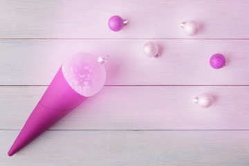 Christmas pink glowing bauble in cone on light wooden background