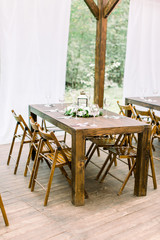 Wedding banquet wooden table in a forest or garden decorated with a composition of white flowers and greenery, lantern