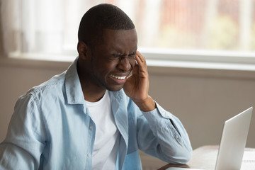 Unhappy tired african american guy suffering from sudden strong headache.