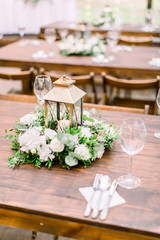 The composition of flowers and greenery, golden lantern in rustic style, standing on served table in the area of wedding party outdoors