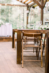 Vintage table setting with floral decorations, white flowers, greenery and lanterns on a wooden floor in restaurant outdoors in garden or forest