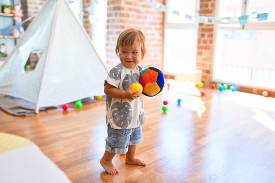 Adorable toddler playing with balls around lots of toys at kindergarten