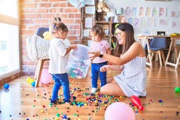 Young beautiful teacher and toddlers playing with building blocks toy at kindergarten