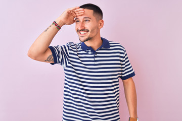 Young handsome man wearing nautical striped t-shirt over pink isolated background very happy and smiling looking far away with hand over head. Searching concept.