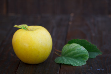 Fresh yellow apple with leaves on wooden background. Organic apple, sweet and healthy fruit.