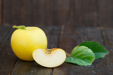 Fresh yellow apple with leaves on wooden background. Organic apple, one cut. Sweet, healthy fruit.
