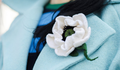 A brooch is a beautiful and fashionable accessory for a woman. Close-up of a girl with beautiful decoration on her neck or outerwear. Bright flower made of fabric - wool, felt. Handwork. handmade