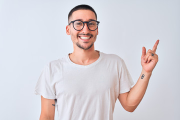Young handsome man wearing glasses and standing over isolated background with a big smile on face, pointing with hand and finger to the side looking at the camera.