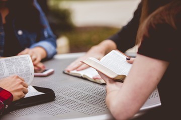 Closeup shot of females sitting around the table reading the bible with a blurred background
