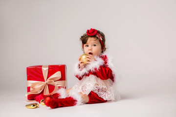 toddler girl Santa with red gift box and Christmas tree toys on white background, space for text