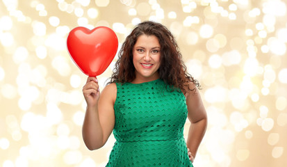 valentine's day, holidays and love concept - happy woman in green dress holding red heart shaped balloon over festive lights on beige background