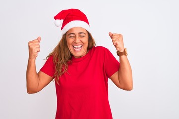 Middle age mature woman wearing christmas hat over isolated background excited for success with arms raised and eyes closed celebrating victory smiling. Winner concept.