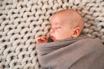 Adorable baby lying down on the sofa over blanket at home. Newborn relaxing and sleeping comfortable