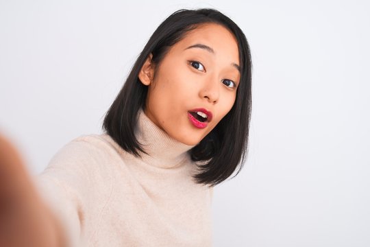 Young chinese woman wearing turtleneck sweater make selfie over isolated white background scared in shock with a surprise face, afraid and excited with fear expression