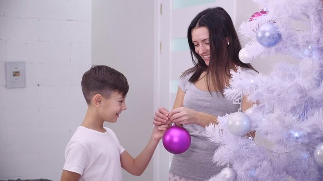 Son and mother decorating a Christmas tree with colourful boubles in the living-room.