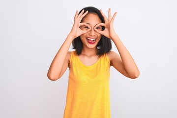 Obraz na płótnie Canvas Young chinese woman wearing yellow casual t-shirt standing over isolated white background doing ok gesture like binoculars sticking tongue out, eyes looking through fingers. Crazy expression.