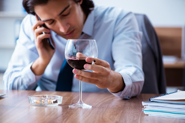Male employee drinking alcohol and smoking cigarettes at workpla