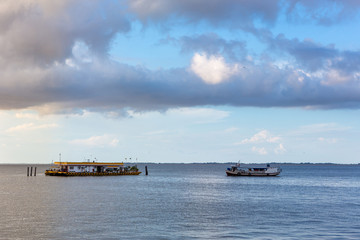 Wooden traditional boat approaches floating gas station in sunny summer day with blue sky and big clouds on Tapajos River, Amazon, Brazil. Transportation and environment concept.