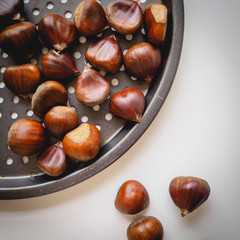Top view of chestnuts in a pan on a white background. Square format.