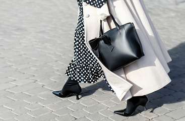 Woman in autumn or spring in a beige coat and a black dress with white polka dots. Fashionable bag...