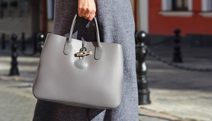 Woman in autumn or spring in a gray coat and gray big bag. Fashionable bag close-up in female hands. Girl walks in the city outdoors. Stylish modern and feminine image, style. . Autumn. Fall colors.