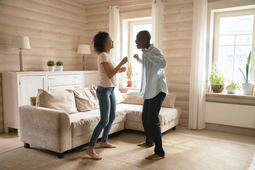 Joyful mixed race family spouse dancing in wooden living room.