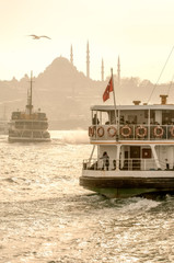 Fototapeta premium Muslim architecture and water transport in Turkey - Beautiful View touristic landmarks from sea voyage on Bosphorus. Cityscape of Istanbul at sunset - old mosque and turkish steamboats, view on Golden