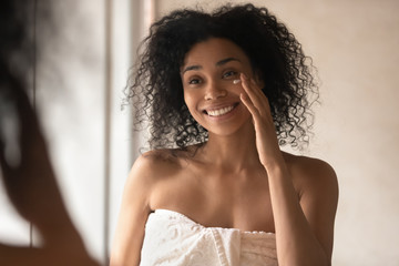Happy african american young woman applying moisturizing balm or cream.