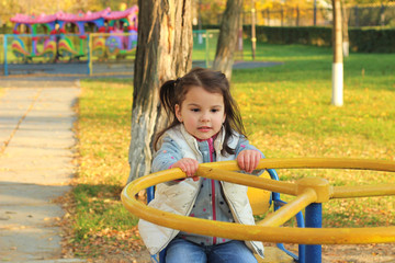 Fototapeta na wymiar White girl with pigtails holds hands on a wheel on a carousel. Autumn playground