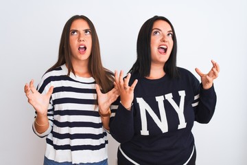 Young beautiful women wearing casual clothes standing over isolated white background crazy and mad shouting and yelling with aggressive expression and arms raised. Frustration concept.