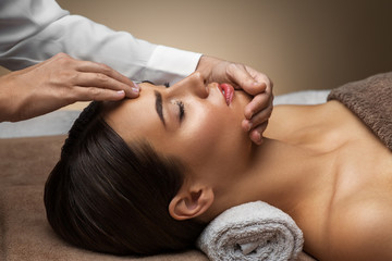 Fototapeta na wymiar wellness, beauty and relaxation concept - beautiful young woman lying with closed eyes and having face and head massage at spa