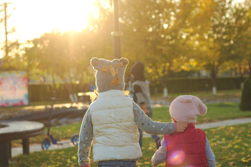 Two children hugging on autumn walk in the park outdoors after playing with fallen leaves in the rays of sunset.