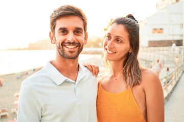 Fototapeta premium Young beautiful couple on vacation smiling happy and confident. Standing with smile on face hugging at the beach