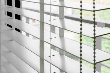 Closeup white color wooden blind with white ladder tape curtains.Sunlight through the windows in the city with garden.Selective focus and light image backdrop.